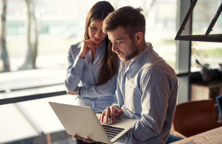 Two colleagues looking at a computer and discussing business.